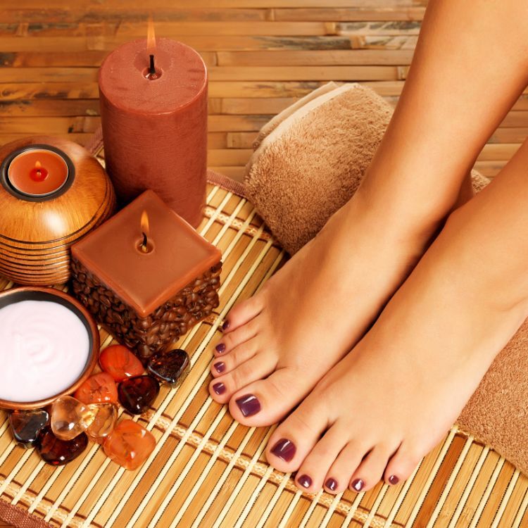 Closeup de pés femininos sobre esteira, com velas, pedras e toalha em spa