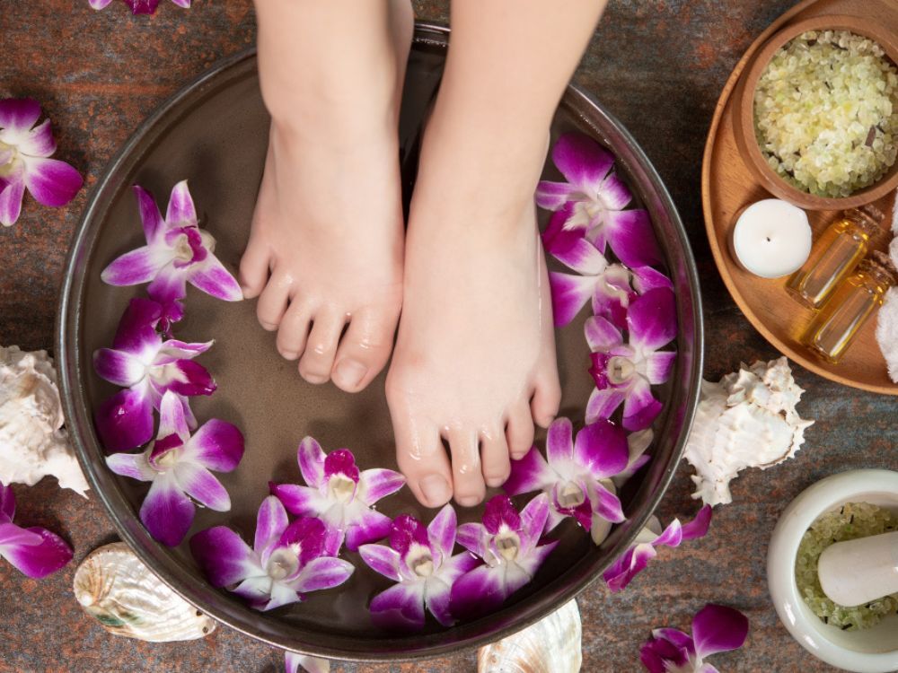 Pés femininos em escalda-pés. Bacia com água e com pétalas de flores